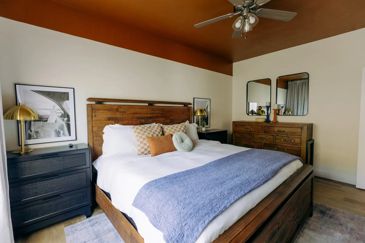 This welcoming bedroom features an inviting bed, dressers, mirrors, and a nightstand. The space is softly lit and exudes warmth and comfort, making it suitable for any guest or family member seeking a restful retreat.