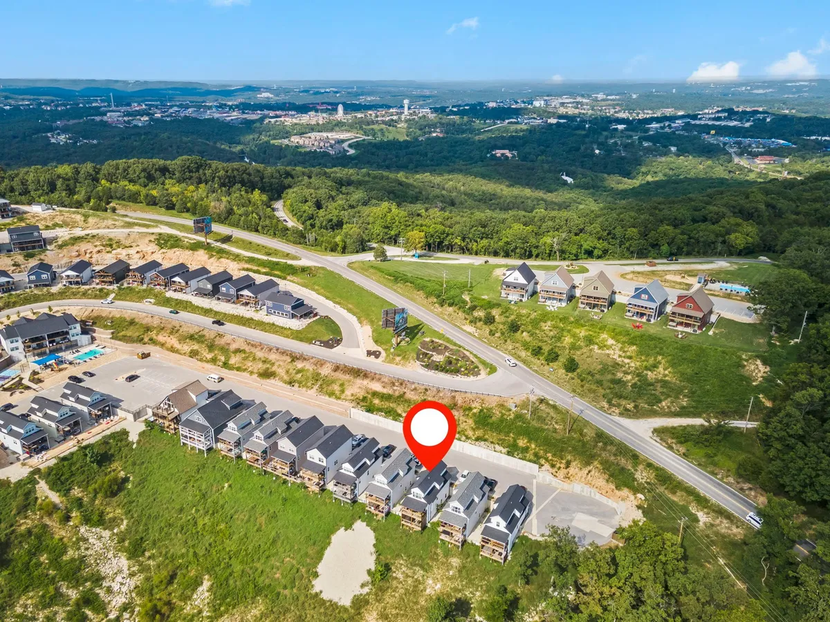 A peaceful scene featuring a row of modern townhouses along a winding road bordered by lush greenery. The distant city skyline is visible, reinforcing the connection to both community and nature. The inviting streetscape suggests a perfect setting for dog walks and outdoor exploration.
