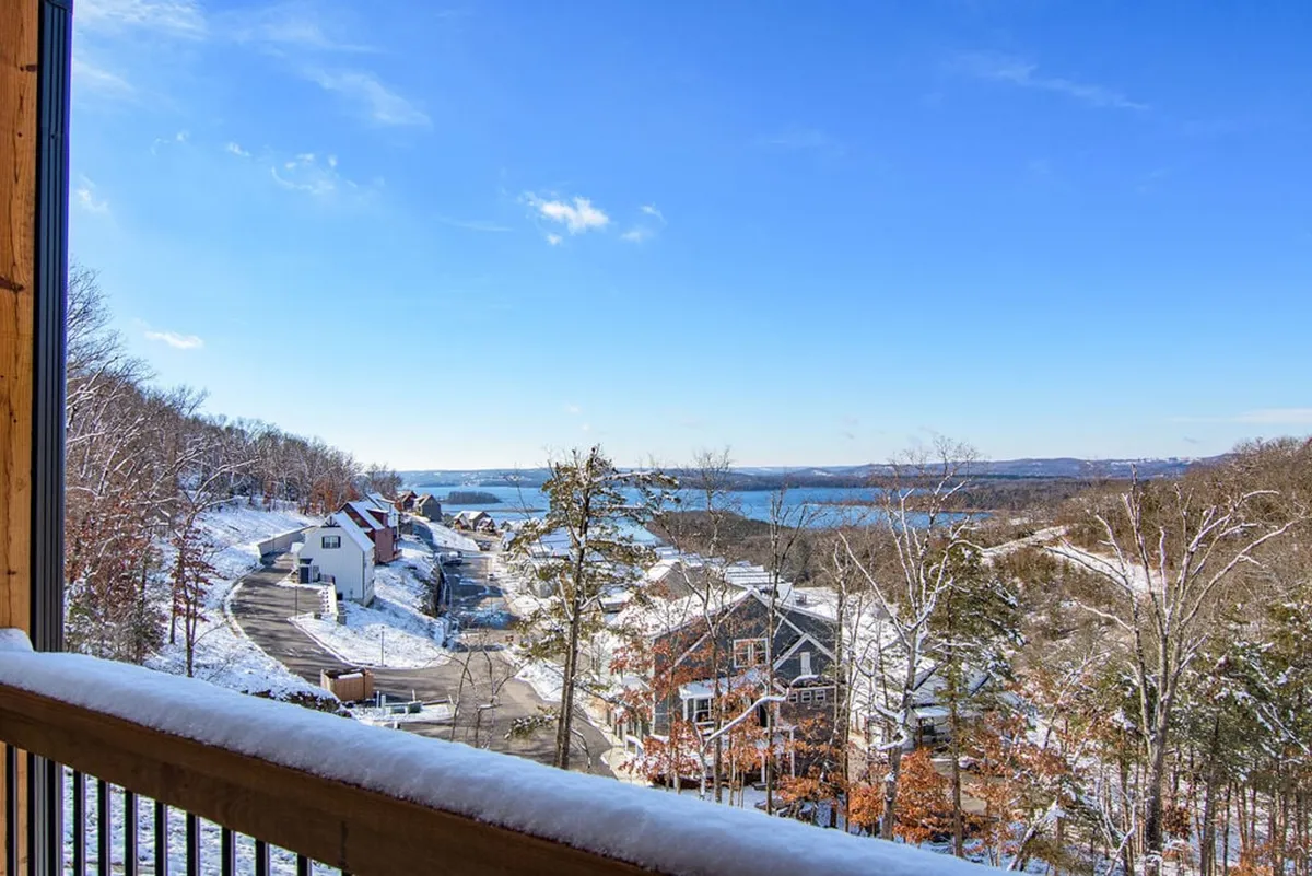 A tranquil, wide view of the community in winter, featuring snow-covered landscapes, a distant lake, a tree line, and residential houses. The scene feels peaceful yet lively, inviting thoughts of cozy indoor gatherings and outdoor exploration during colder months.