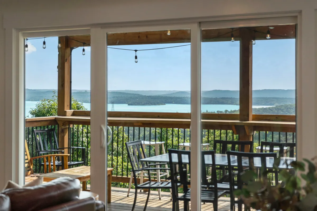 This image features an inviting wooden deck overlooking the lake, with cozy outdoor seating and string lights suspended above. The tranquil setting is perfect for evening relaxation or lively gatherings, with the water and surrounding greenery creating a scenic backdrop.