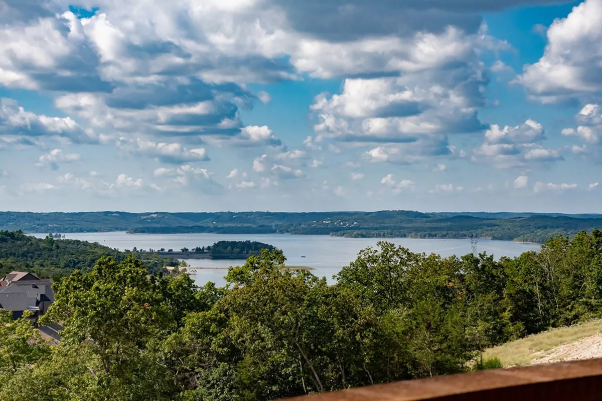 A wide, tranquil view of the lake surrounded by rolling hills and trees under a cloudy sky. The calm water and natural setting evoke the spirit of outdoor adventure, relaxation, and water-based activities like boating and fishing.