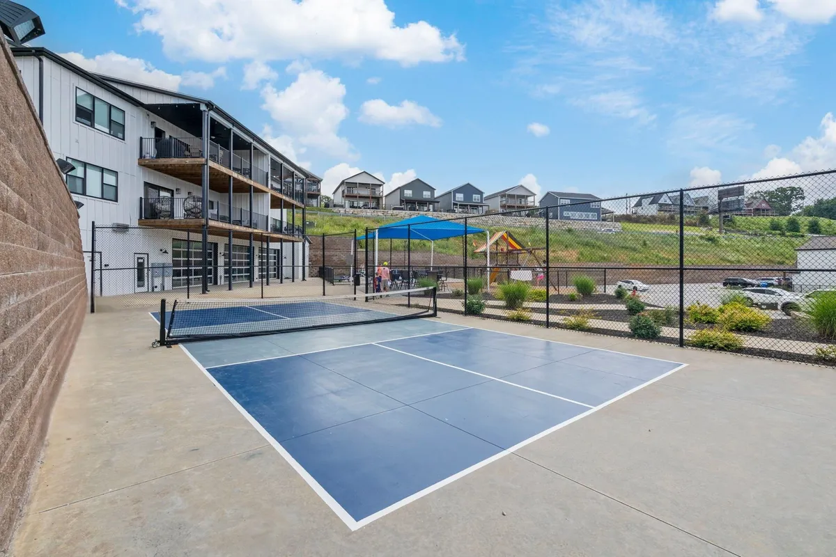 An inviting exterior view that brings the community’s tennis courts, playground, and residential buildings into focus. The courts are ready for friendly matches, and the playground is designed for children to explore. The overall mood is active and communal, with plenty of space for various outdoor activities.