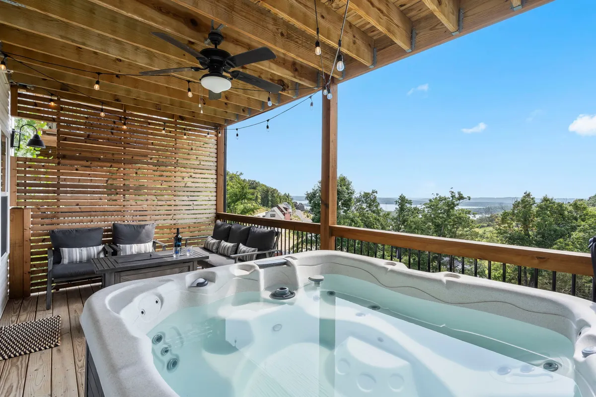 An inviting outdoor scene with a private hot tub nestled on a wooden deck, surrounded by outdoor seating and set against a scenic backdrop. String lights hang above, creating a magical ambiance for evening relaxation.