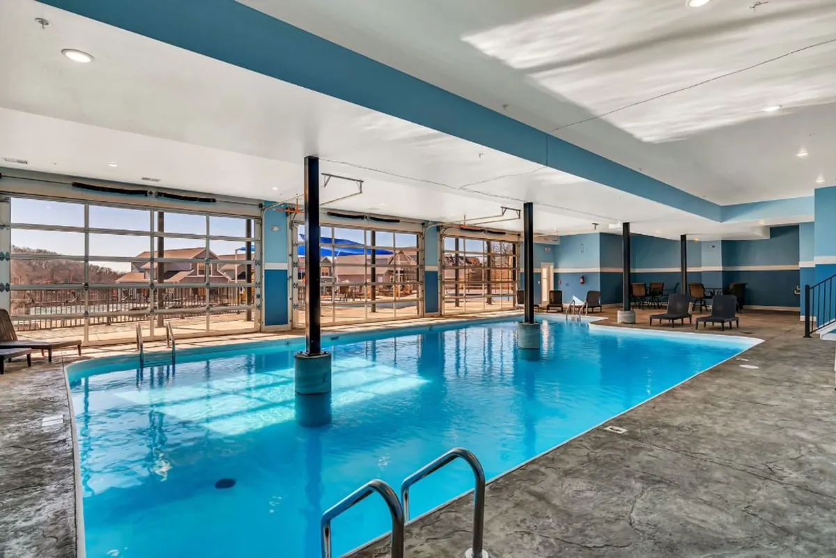 An interior image of an indoor swimming pool with large windows, comfortable seating nearby, and natural light flooding the space. The area is calm and offers spaces for swimming and relaxation.